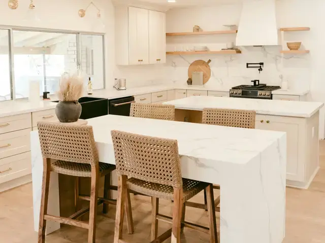 A bright remodeled kitchen with a marble island and woven stools